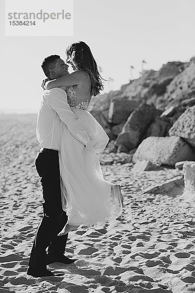 Glückliche Braut und Bräutigam beim Umarmen am Strand