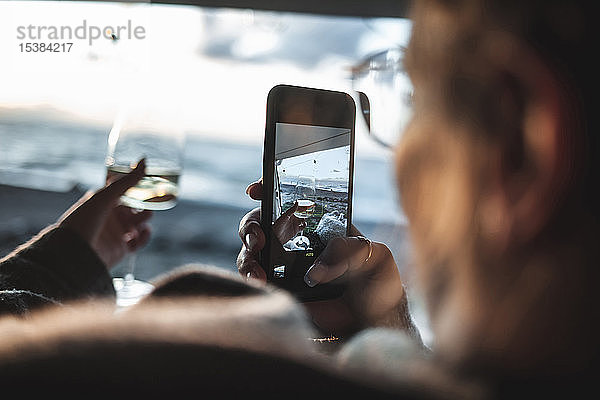 Frau fotografiert ein Glas Weißwein mit ihrem Smartphone am Strand