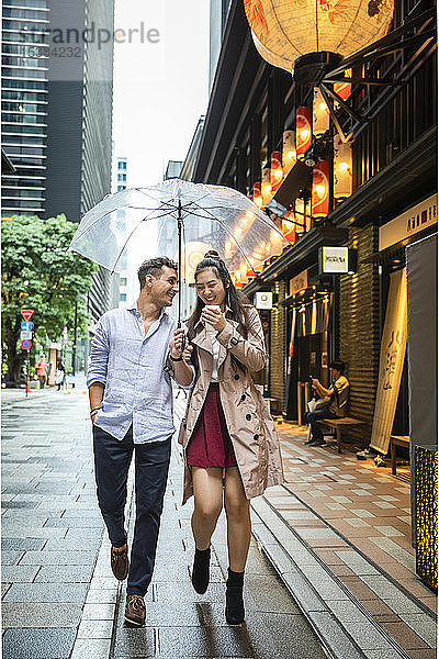 Glückliches Paar mit Regenschirm beim Spaziergang in Ginza  Tokio  Japan