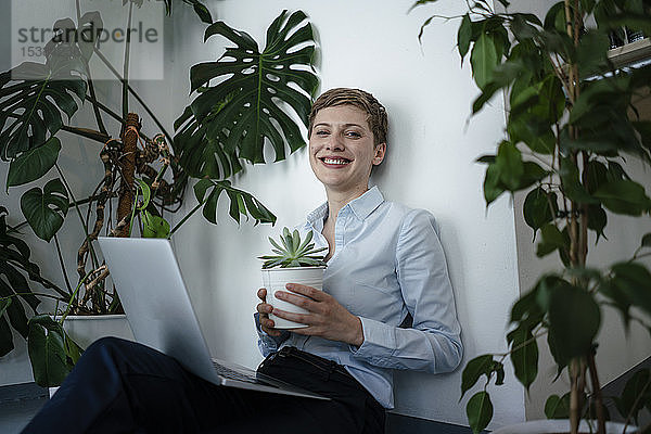 Porträt einer Geschäftsfrau mit Laptop auf dem Boden sitzend  umgeben von Pflanzen
