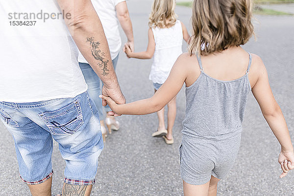 Rückansicht einer Familie  die Hand in Hand auf einer Straße geht