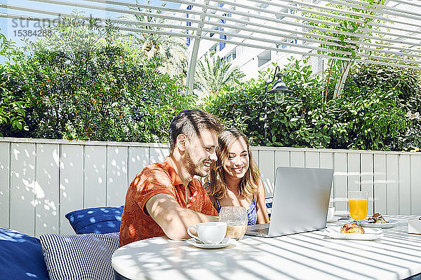 Fröhliches junges Paar benutzt Laptop während des Frühstücks