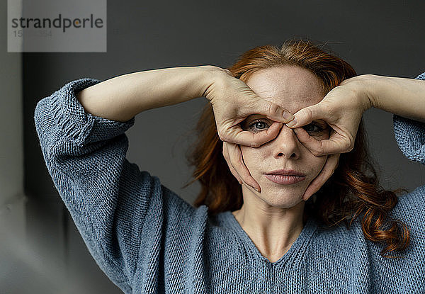 Porträt einer rothaarigen Frau  die mit den Fingern eine Brille formt