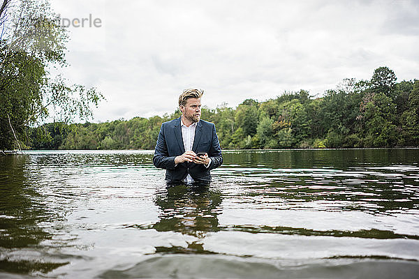 Geschäftsmann steht mit Handy in einem See