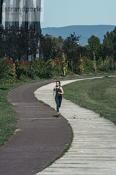 Junge Frau joggt in einem Park auf einem rot-weißen Weg