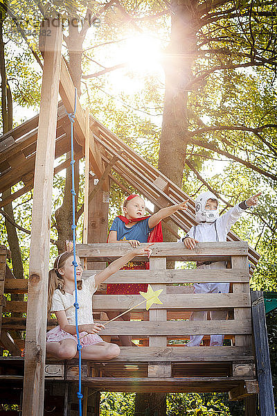 Drei Kinder mit Superhelden-Kostümen spielen auf ihrem Baumhaus