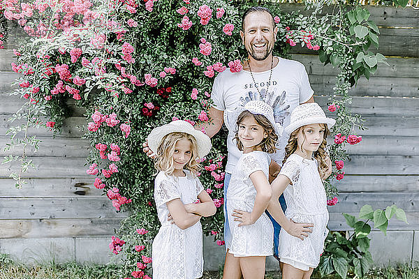 Glücklicher Vater mit drei Drillingsschwestern  die an einem Rosenbusch posieren