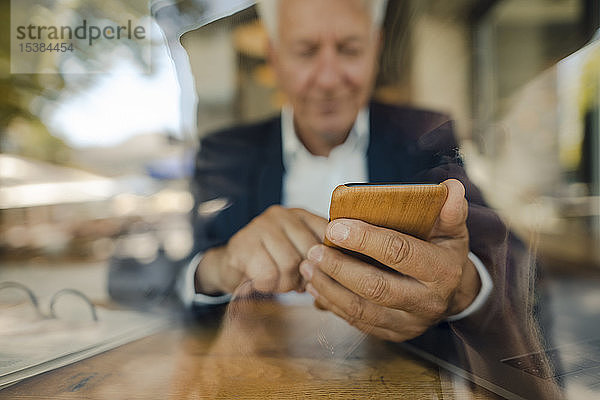 Leitender Geschäftsmann benutzt Mobiltelefon in einem Café