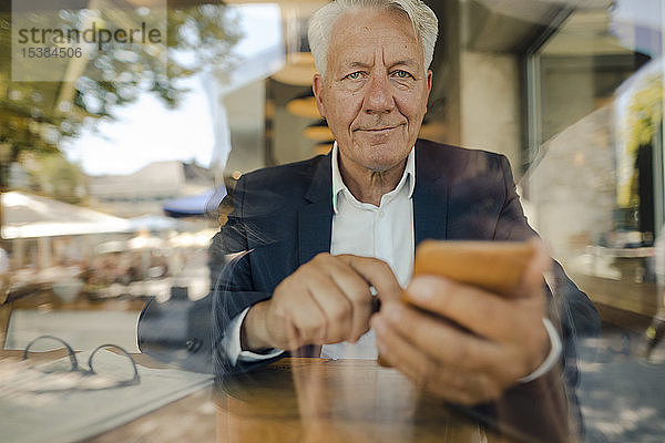 Porträt eines hochrangigen Geschäftsmannes bei der Benutzung eines Mobiltelefons in einem Cafe