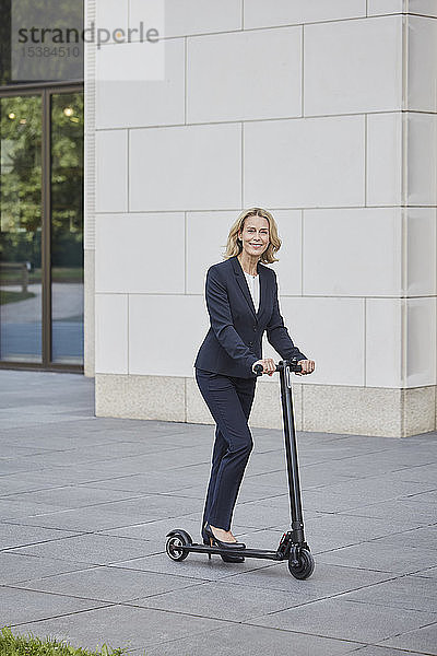 Geschäftsfrau auf E-Scooter vor Bürogebäude in der Stadt
