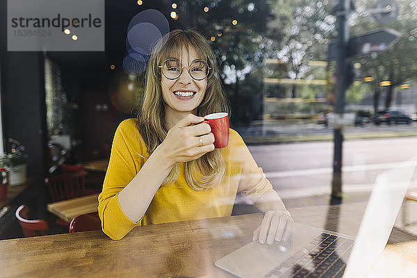 Porträt einer lächelnden Frau mit Laptop und Kaffee in einem Cafe