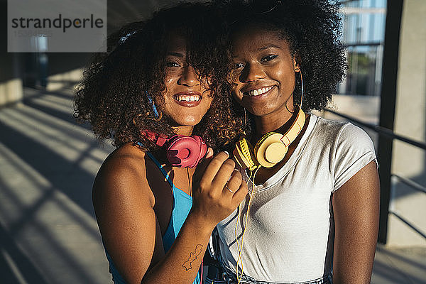 Porträt von zwei glücklichen jungen Frauen mit Kopfhörern in der Abenddämmerung