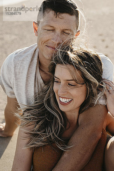 Glückliches  anhängliches junges Paar am Strand