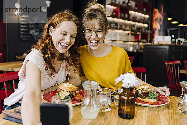 Zwei glückliche Freundinnen beim Burger essen und ein Selfie in einem Restaurant