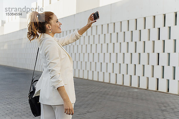 Geschäftsfrau im weißen Hosenanzug  nimmt Smartphone-Selfie
