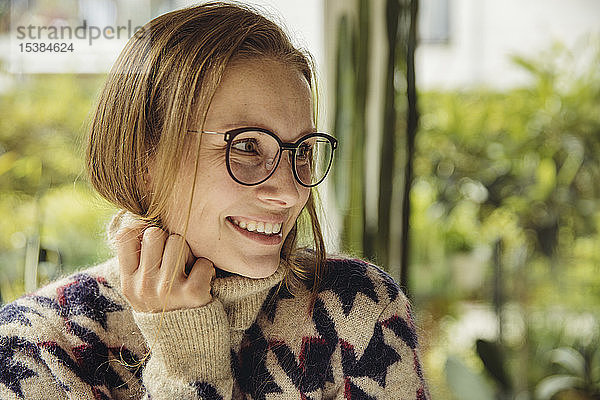 Porträt einer lächelnden jungen Frau mit Brille  die einen flauschigen Pullover trägt und zur Seite schaut