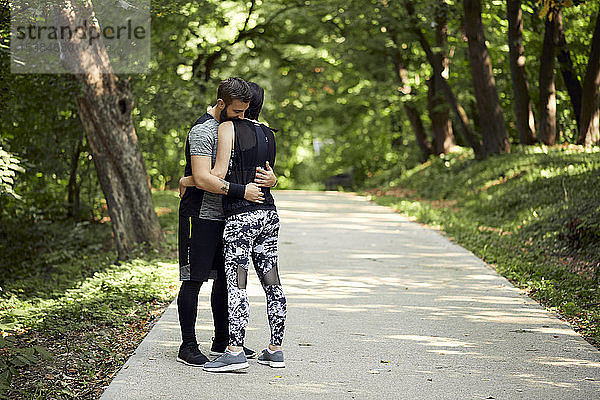 Sportliches Paar umarmt sich auf Waldweg