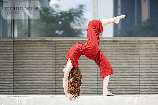 Sportliche junge Frau macht Akrobatik an einer Betonwand