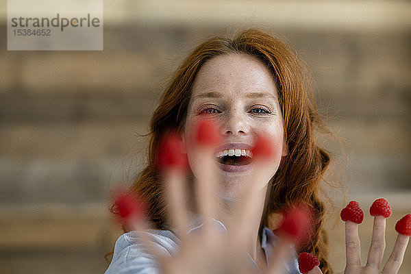 Porträt einer lachenden rothaarigen Frau mit Himbeeren an den Fingerspitzen