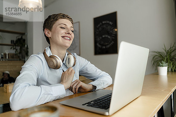 Glückliche Geschäftsfrau mit Laptop und Kopfhörern in einem Cafe