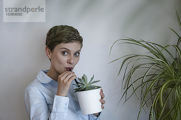Porträt einer Geschäftsfrau  die aus Topfpflanzen trinkt