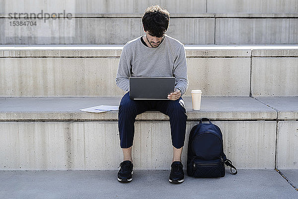 Mann sitzt mit Laptop auf einer Außentreppe