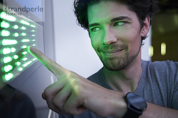 Nahaufnahme eines lächelnden Mannes  der einen grün geführten Touchscreen berührt