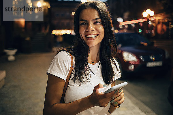 Junge Frau benutzt nachts in der Stadt ein Smartphone