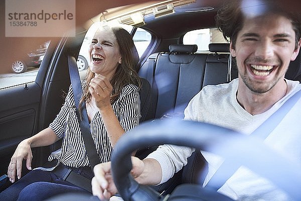 Lachendes Paar in einem Auto mit fahrendem Mann