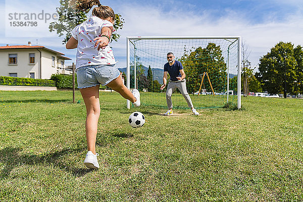 Vater und Tochter spielen auf einer Wiese Fussball
