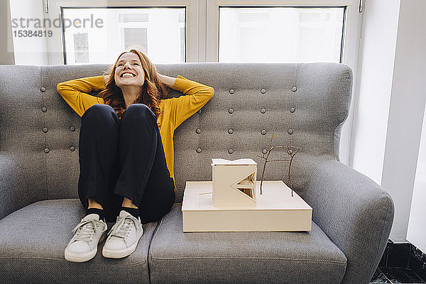 Glückliche Frau sitzt auf dem Sofa neben einem Architekturmodell