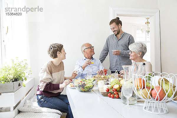 Glückliches älteres Ehepaar mit erwachsenen Kindern beim Mittagessen zu Hause