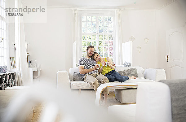 Glückliches junges Paar sitzt zu Hause auf dem Sofa
