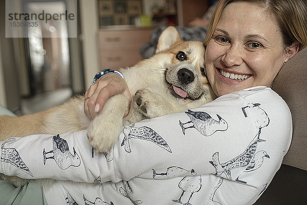 Porträt einer glücklichen Frau  die zu Hause mit ihrem Hund kuschelt