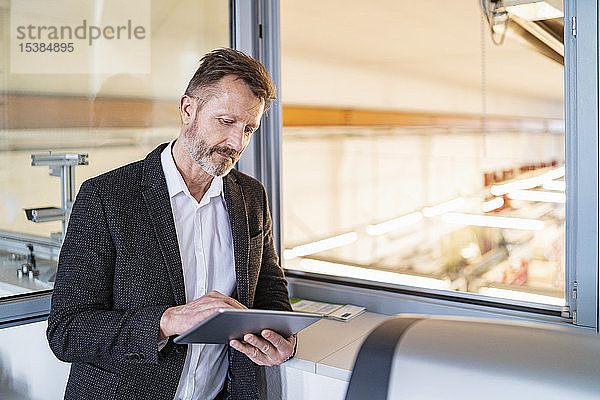 Geschäftsmann mit Tablett am Fenster mit Fabrikhintergrund