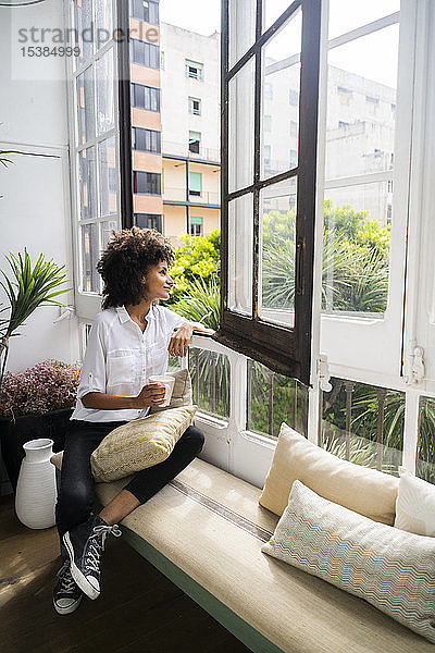 Schöne Frau sitzt auf einer Bank  schaut aus dem Fenster und trinkt Kaffee
