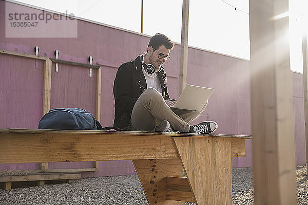 Junger Mann sitzt mit Laptop auf dem Bahnsteig