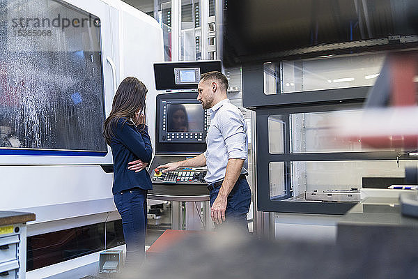 Geschäftsmann und Geschäftsfrau im Gespräch an einer Maschine in einer modernen Fabrik
