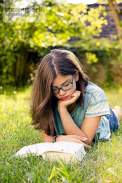 Mädchen liegt auf einer Wiese im Garten und liest Buch