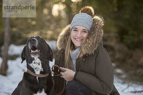 Porträt einer glücklichen jungen Frau mit Hund im Winterwald
