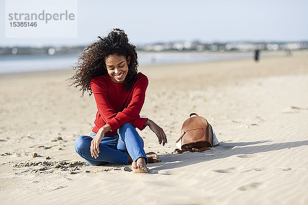 Glückliche junge Frau sitzt am Strand
