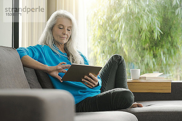 Portrait einer reifen Frau  die zu Hause auf der Couch sitzt und ein digitales Tablet benutzt