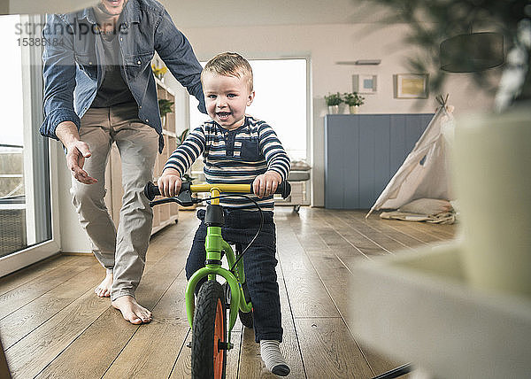 Vater hilft Sohn beim Fahren mit einem Balance-Fahrrad zu Hause
