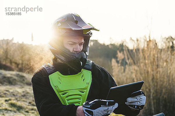 Porträt eines Motocross-Fahrers  der bei Sonnenuntergang auf das Tablet schaut