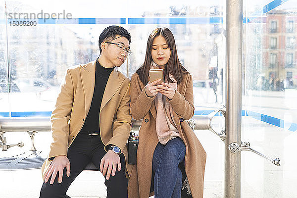 Spanien  Madrid  junges Paar  das am Bahnhof sitzt und in der Stadt mobil telefoniert