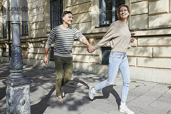 Glückliches Paar rennt auf dem Bürgersteig in der Stadt