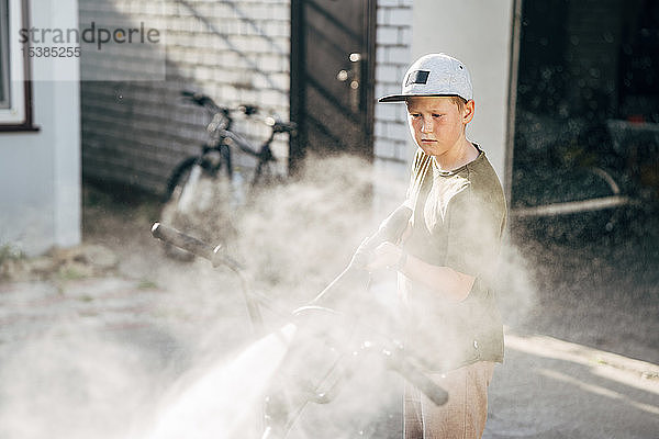 Junge wäscht bmx Fahrrad mit Hochdruckreiniger auf dem Hof