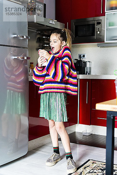 Aufgeregtes Mädchen in gestreiftem Pullover in der heimischen Küche beim Schokoladenessen