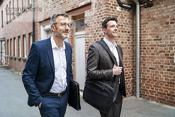 Zwei lächelnde Geschäftsmänner gehen an einem alten Backsteingebäude vorbei