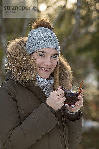 Porträt einer lächelnden jungen Frau  die im Winter Tee trinkt